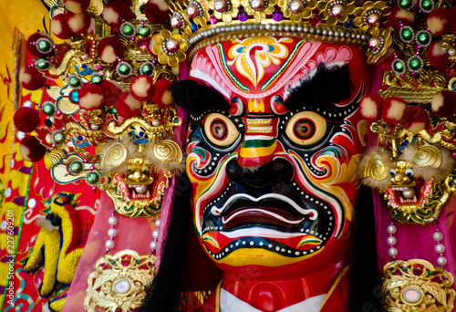 Colorful face of a Chinese deity. The face of the diety and the head ornament are refined pieces of artwork. There are red, pink, yellow, white, yellow, blue and green colors on it. 