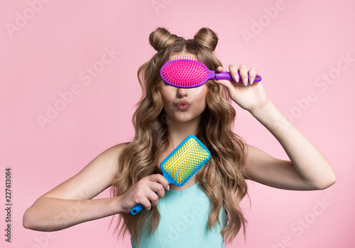 A woman holds a hairbrush in her hands. Woman on a pink background with curly long hair.