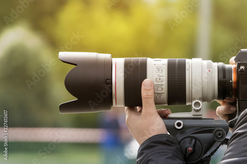 Handshot of a professional photographer outdoors. Man holds a modern camera device. Cameraman shoots outdoors. Shooting with lens. Paparazzi with high-end optical objective. Photographic equipment photo