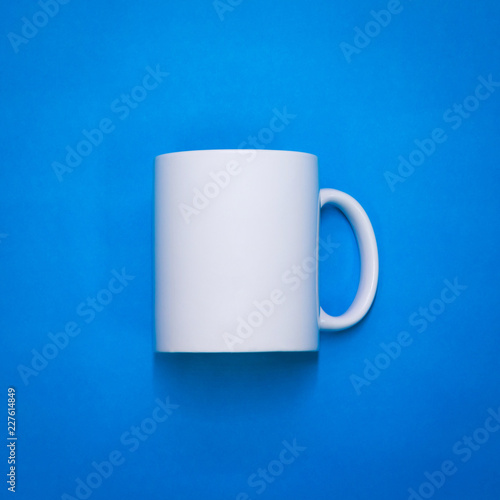 White coffee mug on blue paper background. Template of drink cup for your design. Can put text, image, and logo. Front or side view.