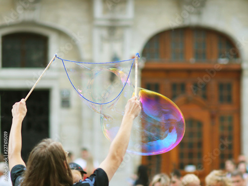 The activator blows huge soap bubbles in the center of the ancient city in front of a joyful crowd. Stick and rope to inflate soapy water. Children's joyful game. Alternative use of foaming agents