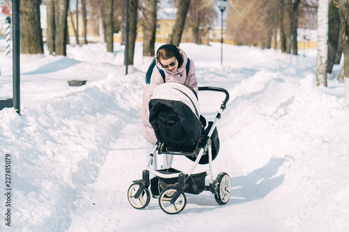 Young mother wlalking with a newborn child in the park in winter. Sunny winter day walk.