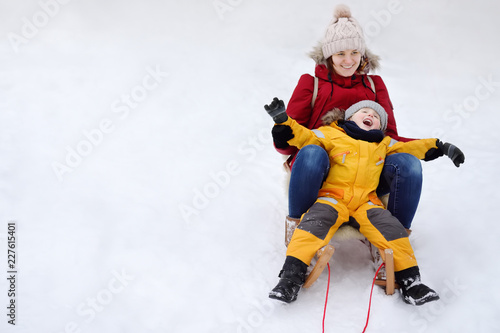Little boy and mother sliding in the park during a snowfall