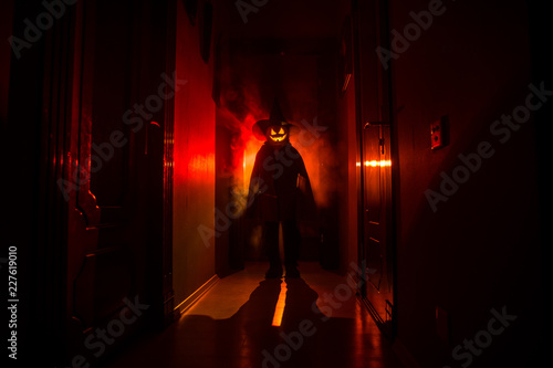 Halloween concept. Creepy silhouette in the dark corridor with pumpkin head. Toned light with fog on background. Selective focus