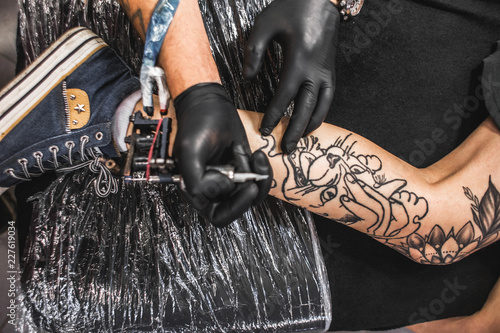 girl with dreadlocks in a tattoo parlor. The master creates a picture on the body of a young beautiful girl. Close-up of hands and tattoo machine