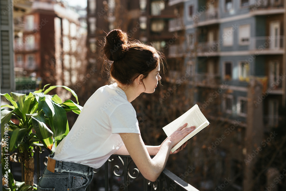 © Bonninstudio/Stocksy - Side view of a young woman reading a book in a balcony. © Bonninstudio/Stocksy - Side view of a young woman reading a book in a balcony.