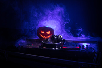 Halloween pumpkin on a dj table with headphones on dark background with copy space. Happy Halloween festival decorations and music concept