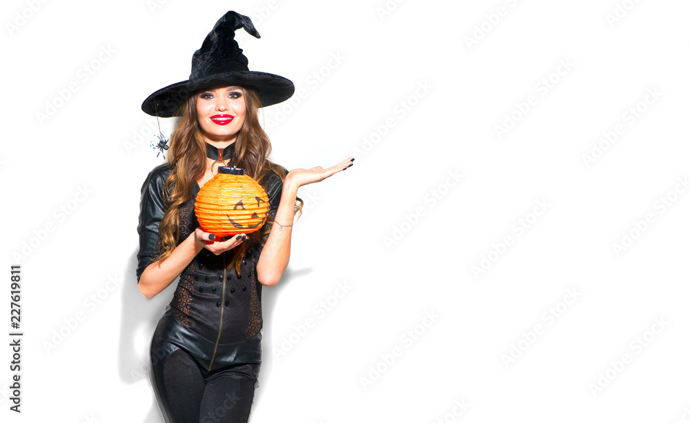 Halloween. Sexy witch with bright holiday makeup. Beautiful young woman in witches costume with pumpkin lantern pointing hand, showing product over white background 
