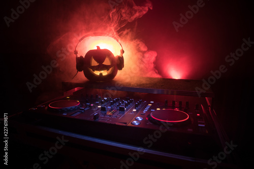 Halloween pumpkin on a dj table with headphones on dark background with copy space. Happy Halloween festival decorations and music concept