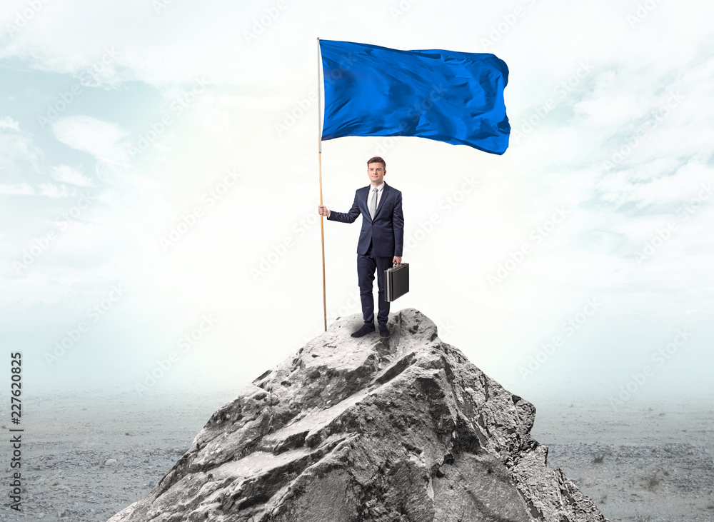 Obraz premium Handsome businessman on the top of the mountain with blue flag 