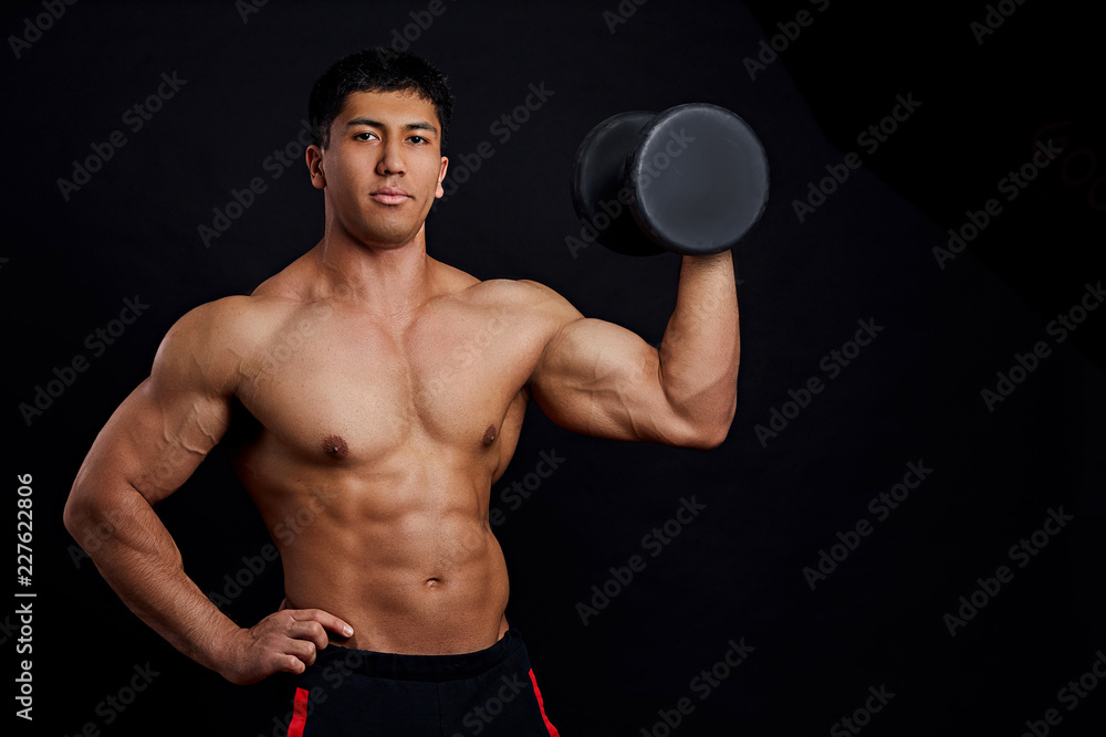 young ambitious man with heavy dumbbell posing to the camera. isolated on the black background. copy space.