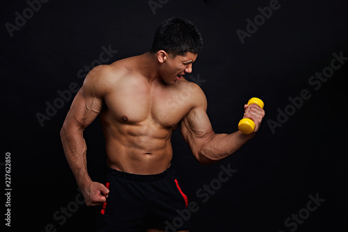 Muscular frustrated angry guy doing exercises with dumbbell over black background. studio shot.tense concept