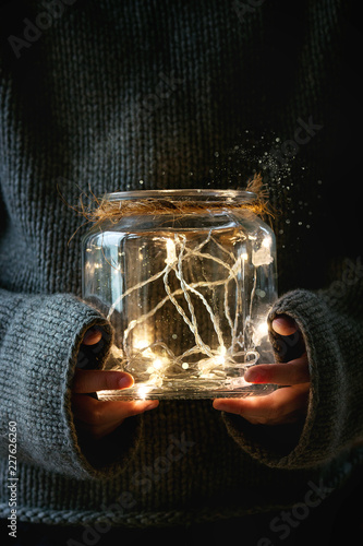 Boy in gray wool pullover holding in arms Christmas lights garland in glass jar. Christmas holiday mood. photo