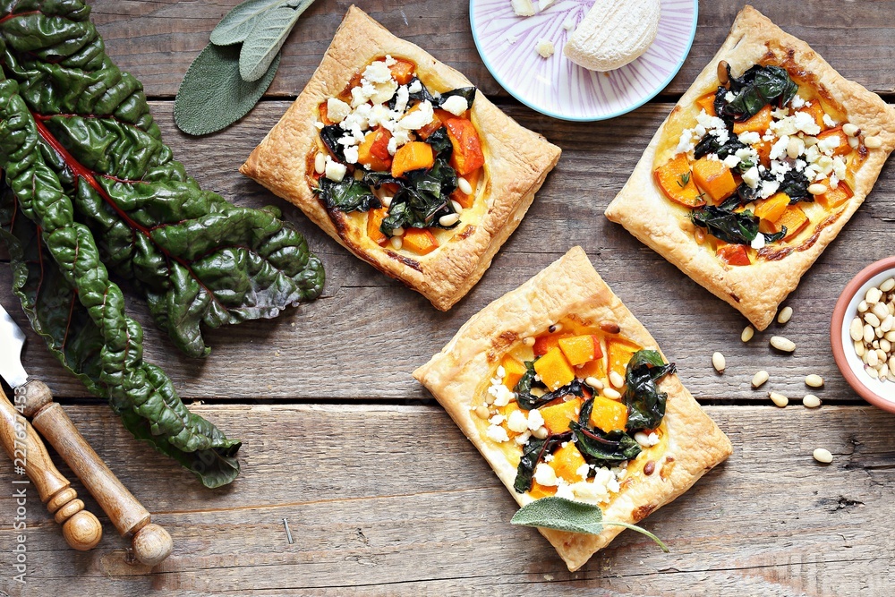 Pumpkin, chard, goat cheese and pine nuts puff pastry tarts. Overhead view Pumpkin, chard, goat cheese and pine nuts puff pastry tarts. Overhead view