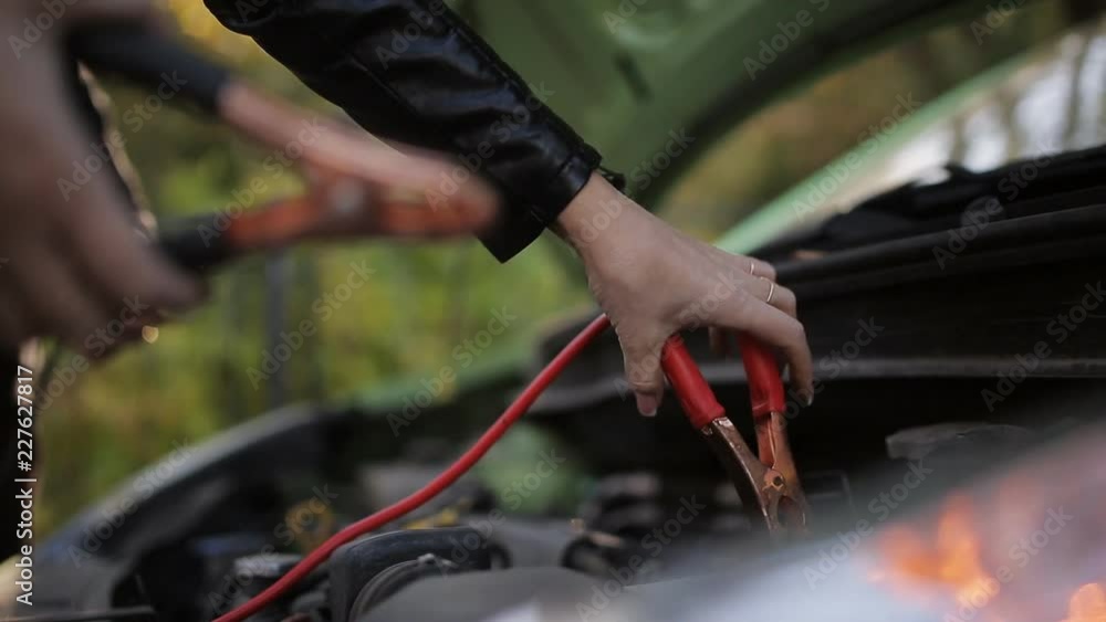 Close-up shot of a girl attaching jumper cables to a battery. Jump Starting a car, detail footage of cables charging a dead battery Close-up shot of a girl attaching jumper cables to a battery. Jump Starting a car, detail footage of cables charging a dead battery