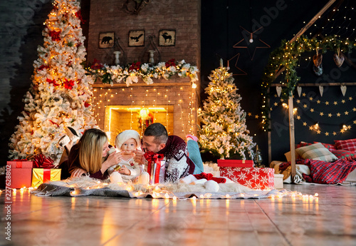 Happy family with a baby in a Santa Claus hat in a Christmas room in Christmas day.