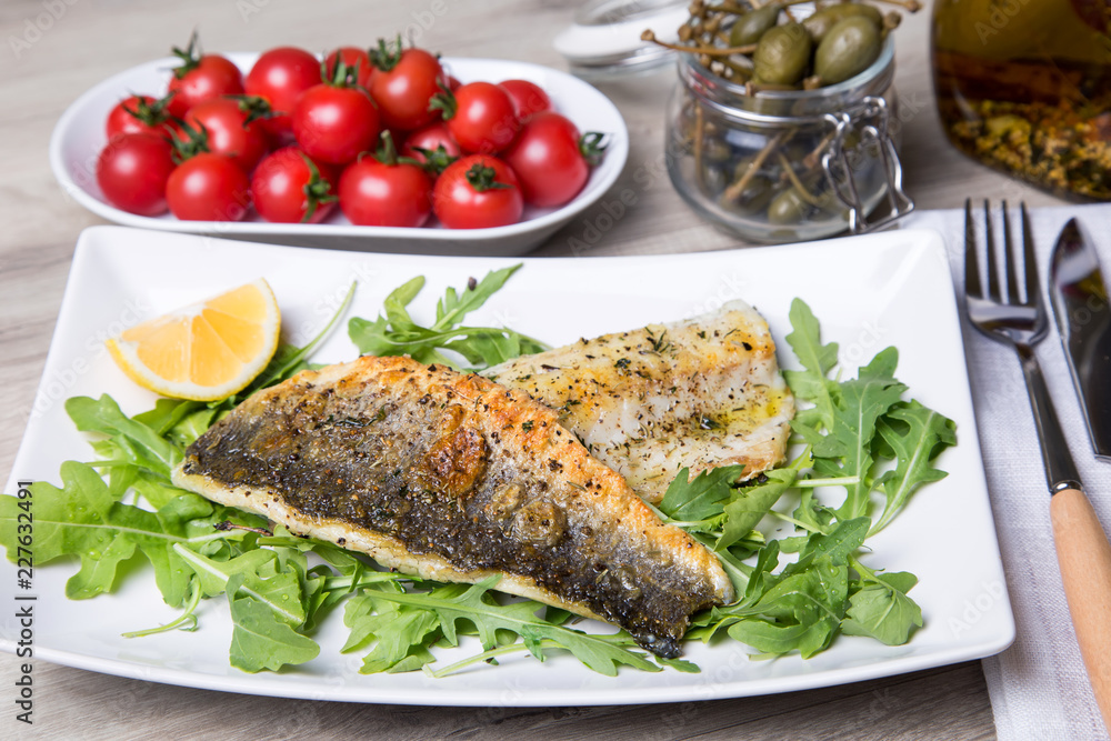 Grilled seabass fillet with arugula, lemon, tomatoes and capers. Close-up. Grilled seabass fillet with arugula, lemon, tomatoes and capers. Close-up.
