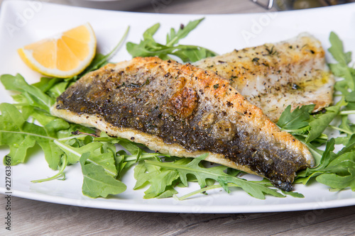 Grilled seabass fillet with arugula and lemon. Close-up.
