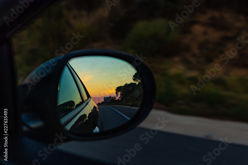 Right mirror driving car on an orange sunset landscape