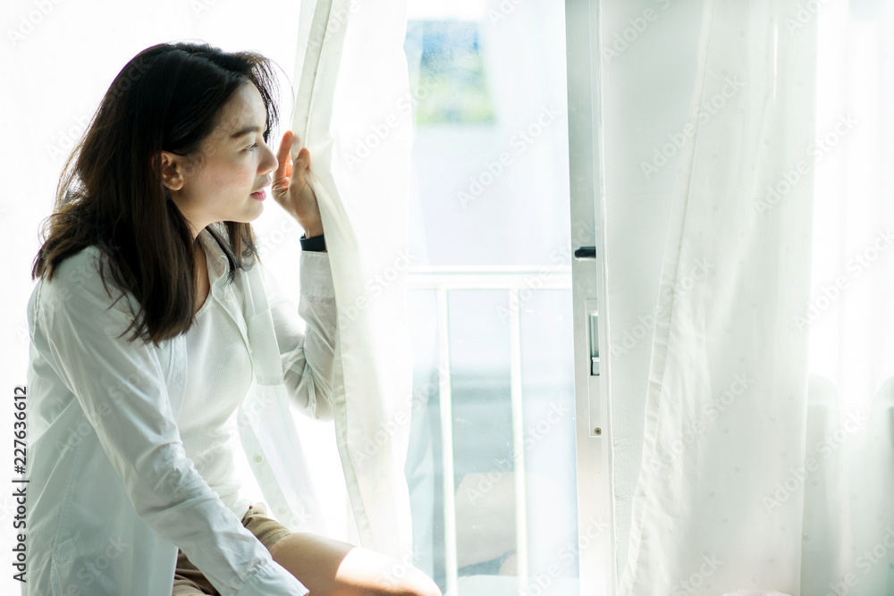 Portrait happy woman looking through of the window in the morning Portrait happy woman looking through of the window in the morning