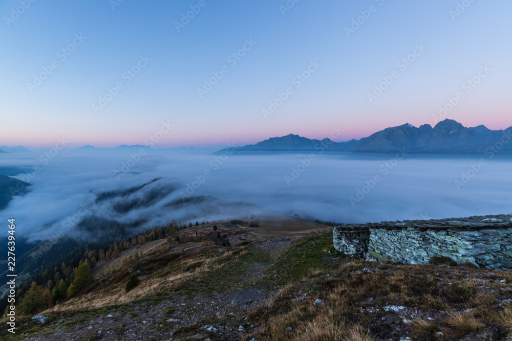Colorful Early Morning Autumn Mountain Panorama View From Mt. Mohar In Nationalpark Hohe Tauern Carinthia To Schober Group and Grossglockner With Fog Down Above The Valley