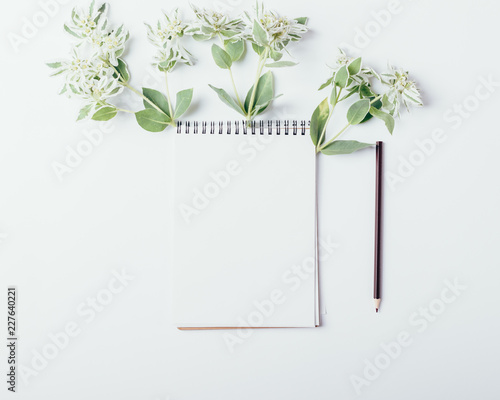 Mock-up with clean notepad and small green flowers