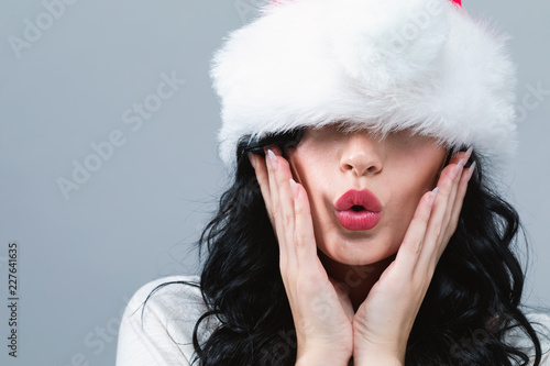 Fototapeta Naklejka Na Ścianę i Meble -  Woman with a Santa hat pulled over her eyes on a gray background