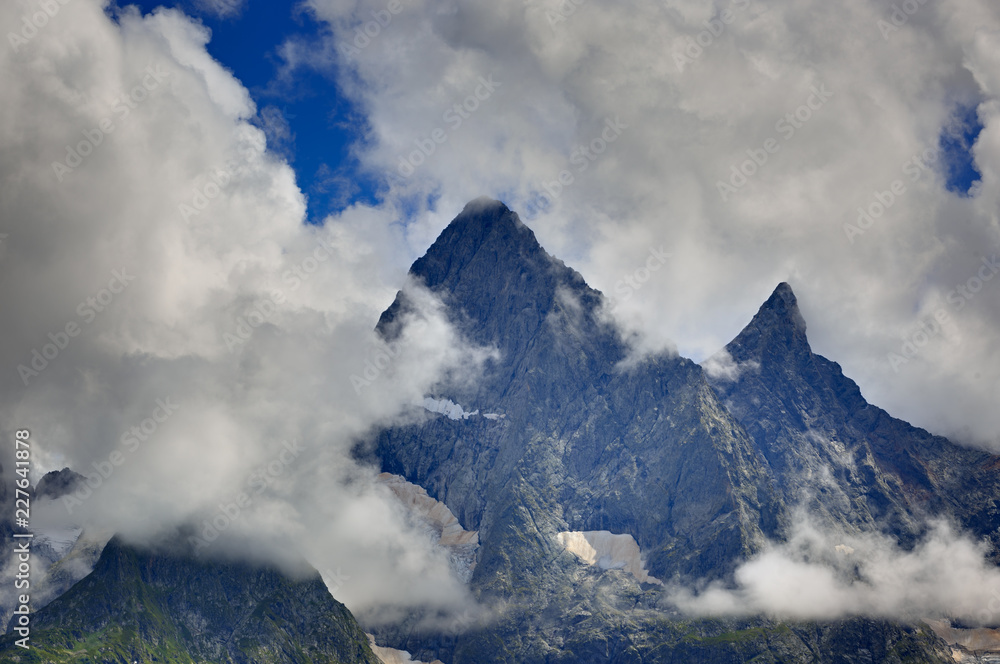 Peak of the mountain with glaciers against the background of clouds and sky. Caucasian ridge, Russia. Peak of the mountain with glaciers against the background of clouds and sky. Caucasian ridge, Russia.