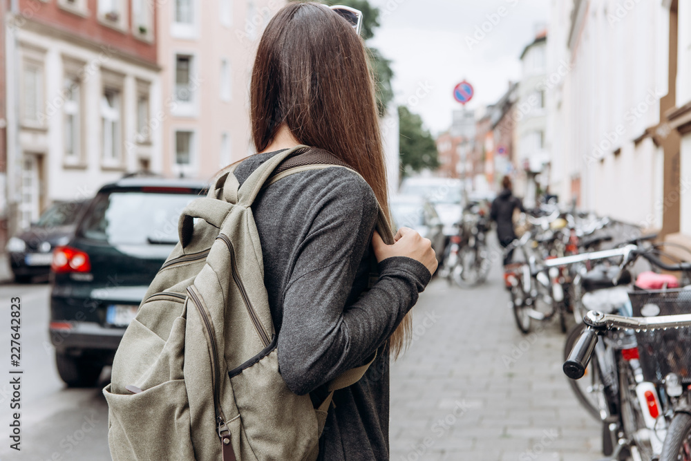 Fototapeta premium Tourist with a backpack is looking for booked online accommodation in an unfamiliar city. Or a student girl with a backpack is walking through the city.