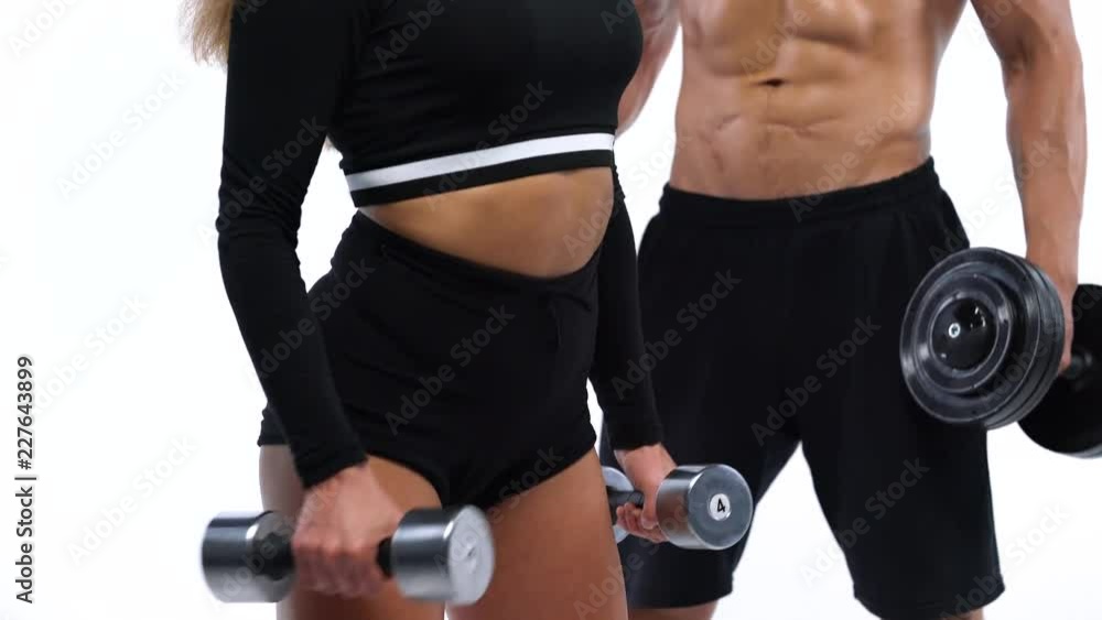 Athletic man and woman flexes their hands with dumbbells, training their biceps on a white background in studio Athletic man and woman flexes their hands with dumbbells, training their biceps on a white background in studio