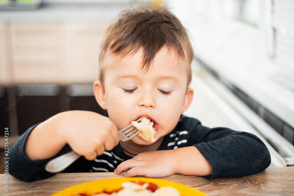 Hungry child eating dumplings in the kitchen, sitting at the table in a gray jacket Hungry child eating dumplings in the kitchen, sitting at the table in a gray jacket