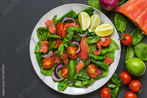 Salmon salad with spinach, cherry tomatoes, red onion and basil in marble plate over dark stone background. healthy food