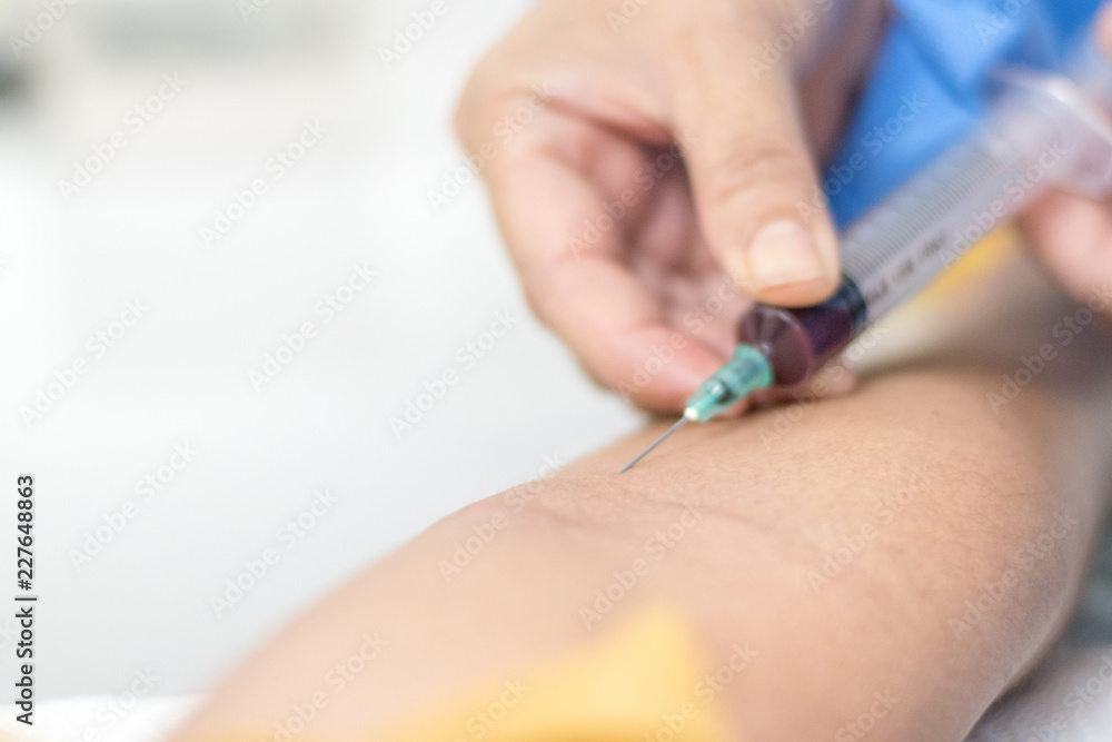 Doctor or nurse hands using needle syringe drawing blood sample from