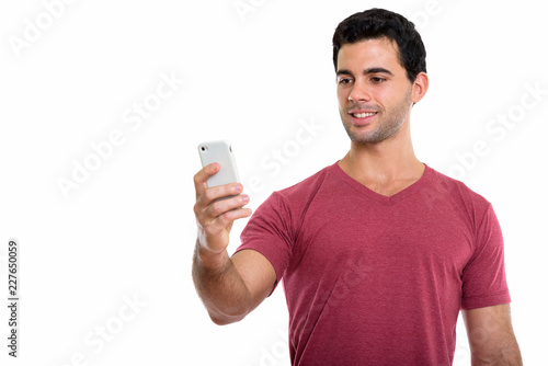 Studio shot of young happy Hispanic man smiling while using mobi