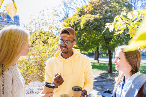 Multi-ethnic group of students drinking coffee to go together outdoors in a college campus, autumn park, city square. photo