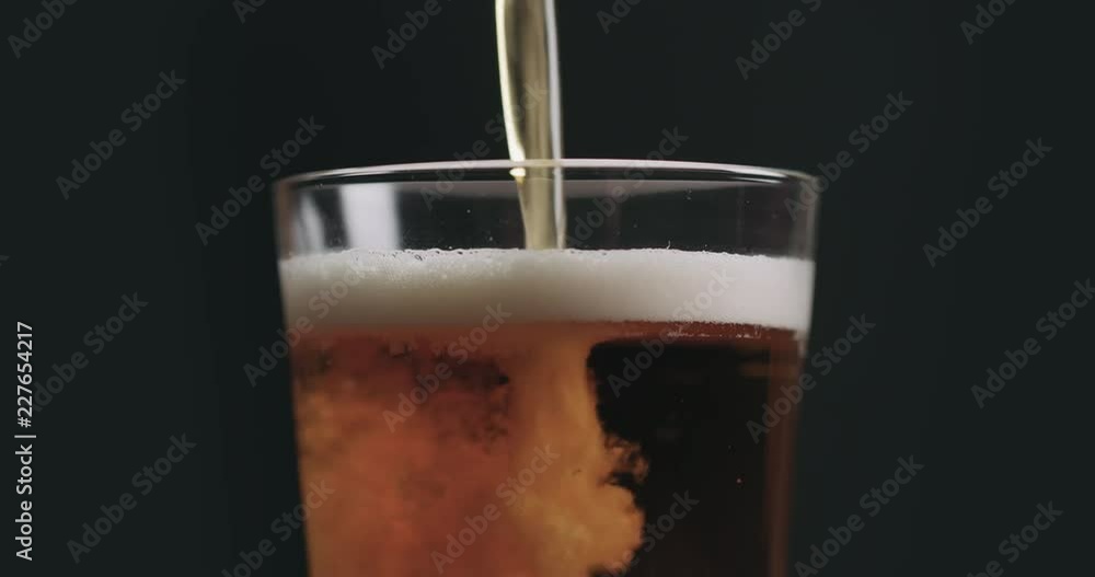 Closeup slow motion pour light ale beer in pint glass over black background Closeup slow motion pour light ale beer in pint glass over black background