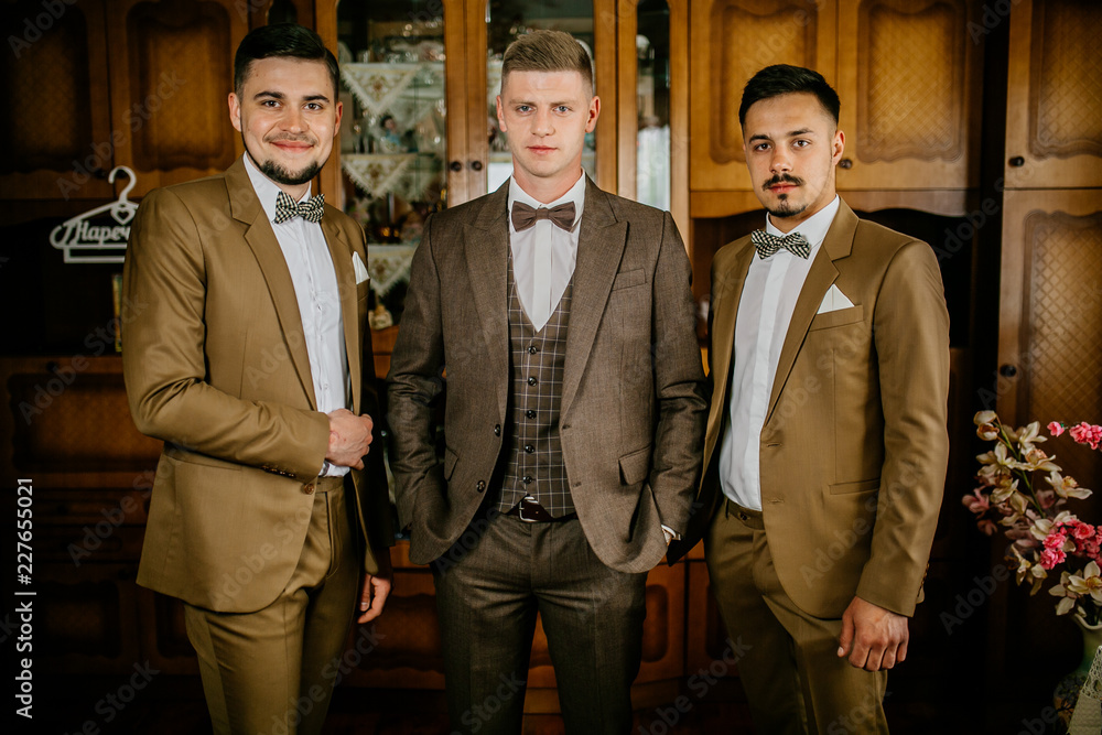 stylish groomsmen helping happy groom getting ready in the morning for wedding ceremony. luxury man in suit in room. Groom preparation before wedding ceremony.