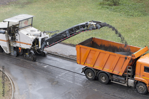 Road milling machine removes old asphalt and loads milled asphalt into the dump truck. Road repair process. High angle view