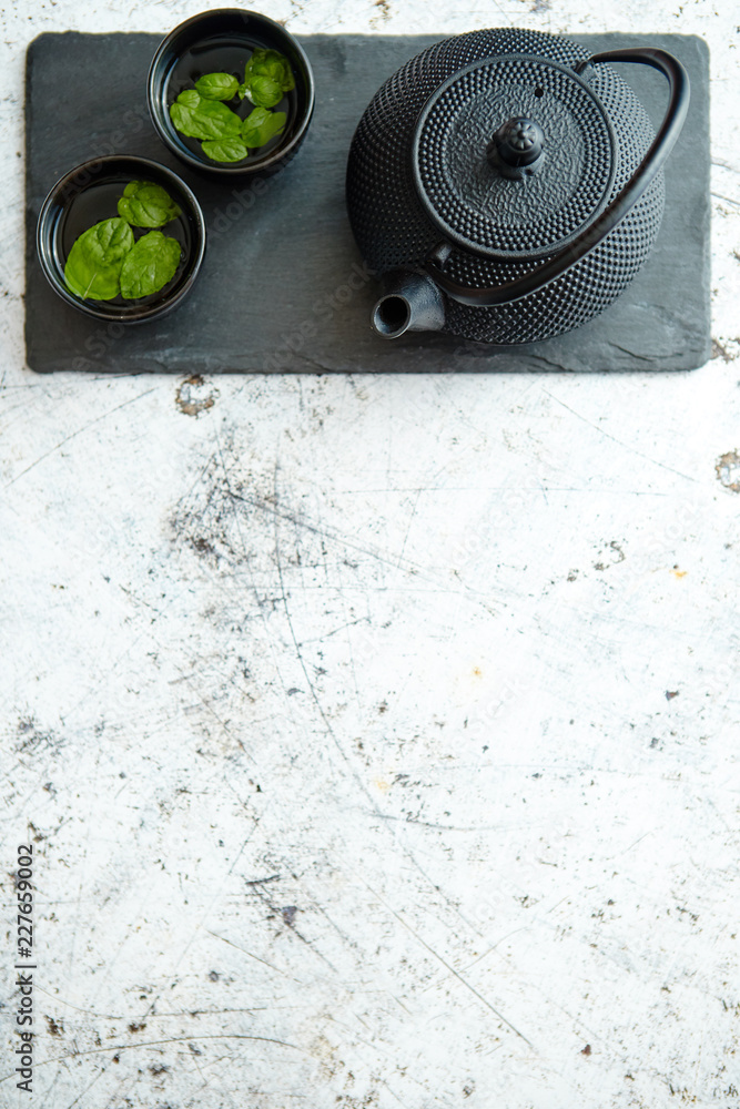 Traditional eastern metal teapot and iron cups with mint tea leafs placed on stone plate. Over the white rusty stone background