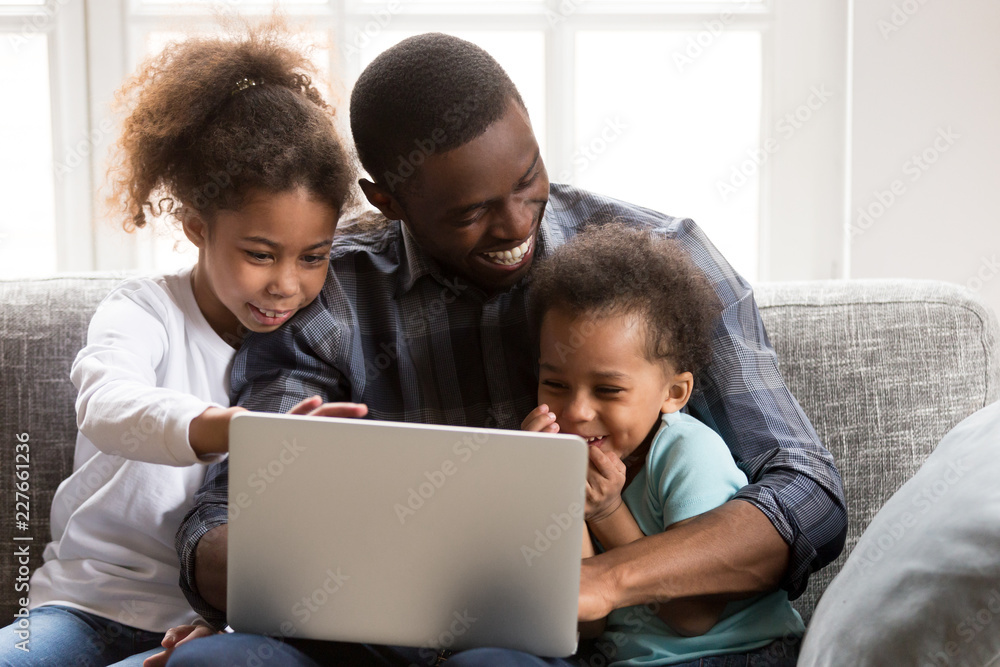 Happy African family spend time have a fun together using computer at home. Black father with little preschool daughter and toddler son watching funny video laughing sitting on couch at sitting room Happy African family spend time have a fun together using computer at home. Black father with little preschool daughter and toddler son watching funny video laughing sitting on couch at sitting room