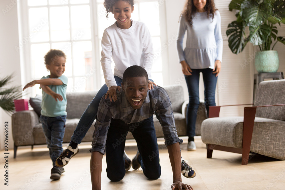 Black African wellbeing attractive family spend free time on weekend have a fun together in living room at new modern home. American happy laughing father rolls little preschool daughter on his back Black African wellbeing attractive family spend free time on weekend have a fun together in living room at new modern home. American happy laughing father rolls little preschool daughter on his back