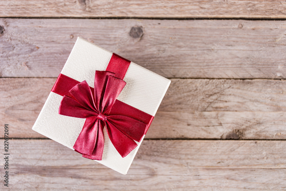 Gift box with red bow on retro wooden desk and space for text and design. Christmas and holiday present concept. Top view, selective focus Gift box with red bow on retro wooden desk and space for text and design. Christmas and holiday present concept. Top view, selective focus