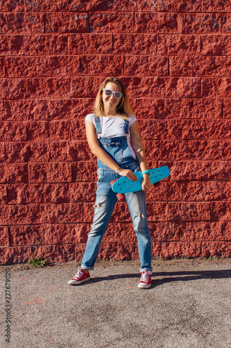 Portrait of a smiling woman standing with her skateboard next to the red wall. © Smile