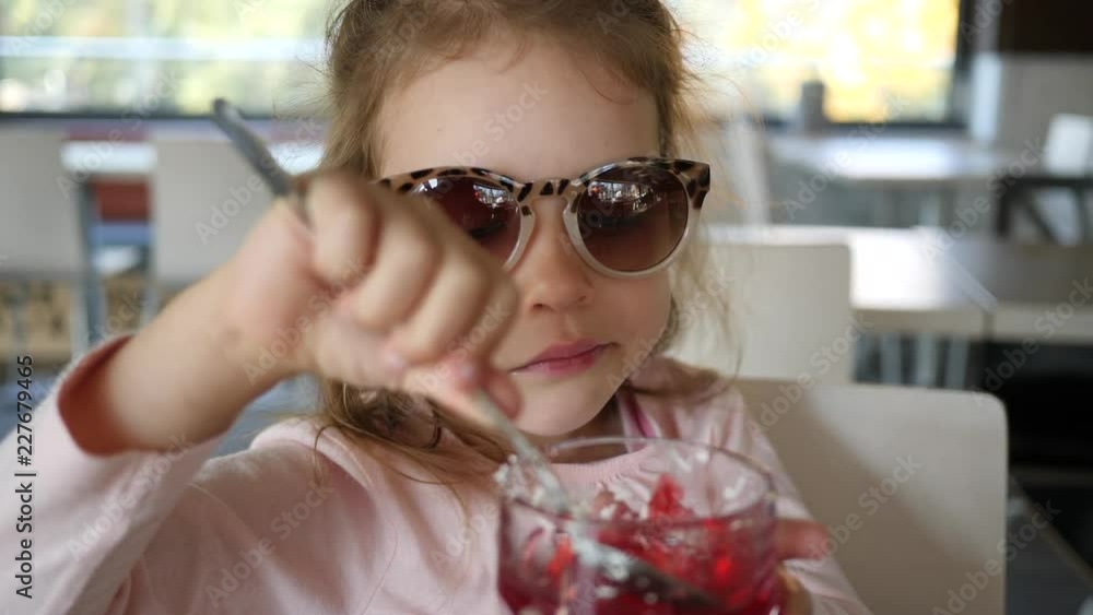 Cute child girl portrait in cafe bistro eating sweet jelly dessert with a spoon Cute child girl portrait in cafe bistro eating sweet jelly dessert with a spoon