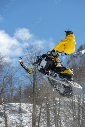 racer on a snow-cat in flight, jumps and takes off on a springboard against the snowy mountains
