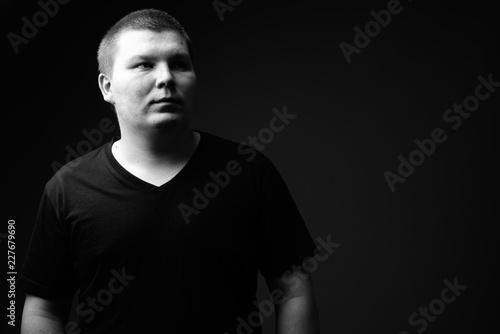 Overweight young man against black background in black and white