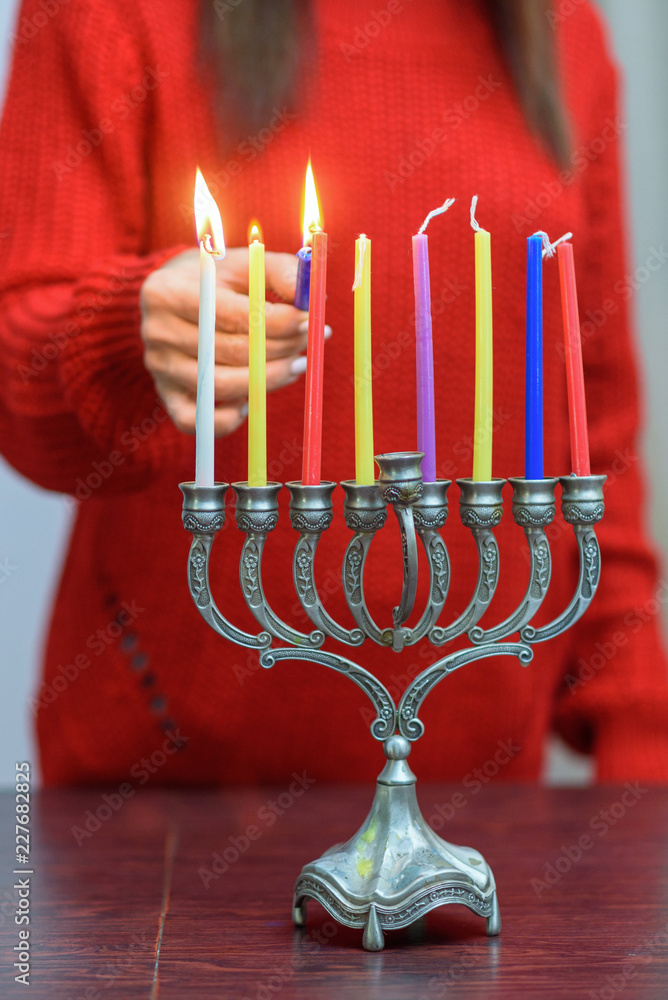 Fototapeta premium Jewish Woman lighting Hanukkah Candles in a menorah. People celebrate Chanukah by lighting candles on a menorah, also called a Hanukiyah. Each night, one more candle is lit.