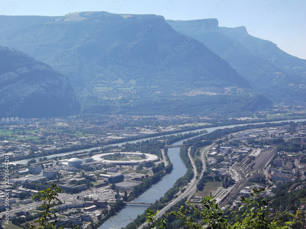 Die französische Stadt Grenoble. Ausblick nach Osten von der Bastille, man erkennt im Zusammenfluss von Isere und Drac ein ringförmiges Gebäude - das Synchrotron ESRF.