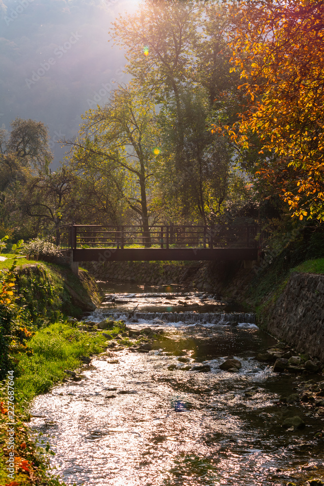 Picturesque view of a wooden bridge over a river or a creek  with waterfalls in autumn with natural lens flare. Autumn river landscape, Samobor near Zagreb, Croatia