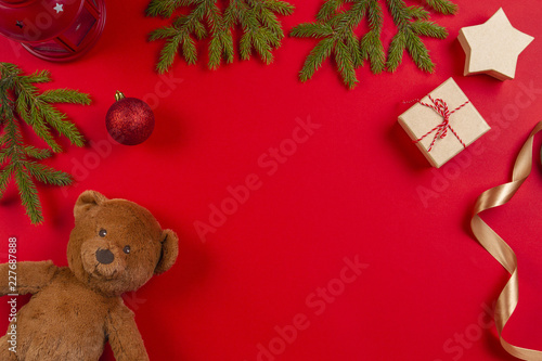Christmas composition. Teddy bear, fir tree branches, christmas decorations and present gift box on red background